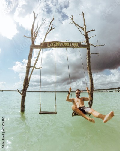 Man on a swing in a fresh water blue lagoon in Bacalar, Mexico.