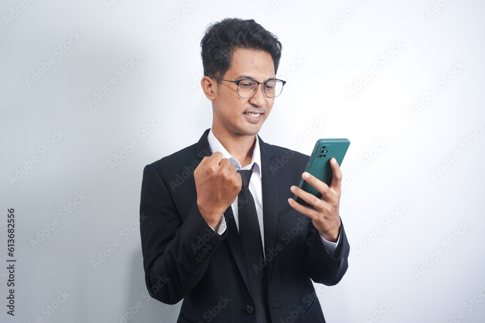 Excited happy young Asian man winner feeling joy using smartphone winning lottery game, betting, getting cashback online gift in mobile app message holding cell phone isolated on white background. Excited happy young Asian man winner feeling joy using smartphone winning lottery game, betting, getting cashback online gift in mobile app message holding cell phone isolated on white background.