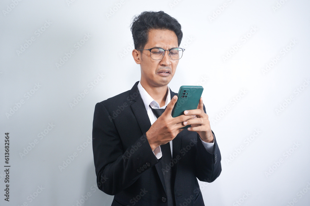 Asian guy wearing a suit looks sad reading online news from his cellphone. man shows disappointed gesture by wiping tears from his face Asian guy wearing a suit looks sad reading online news from his cellphone. man shows disappointed gesture by wiping tears from his face