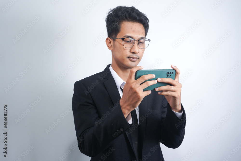 Portrait of a passionate and serious young man in suit playing game on mobile in office isolated over white background Portrait of a passionate and serious young man in suit playing game on mobile in office isolated over white background