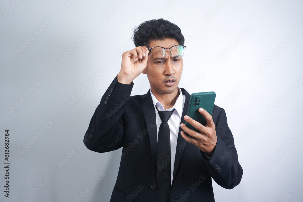 Amazed shocked Asian guy holding smartphone in his hand, looking at the phone in surprise with his glasses raised, stunned facial expression, stands on isolated orange background Amazed shocked Asian guy holding smartphone in his hand, looking at the phone in surprise with his glasses raised, stunned facial expression, stands on isolated orange background