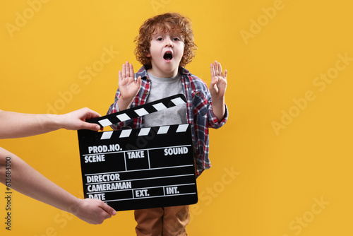 Emotional cute boy performing while second assistant camera holding clapperboard on orange background. Little actor