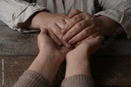 Woman holding hands with her mother at wooden table, closeup