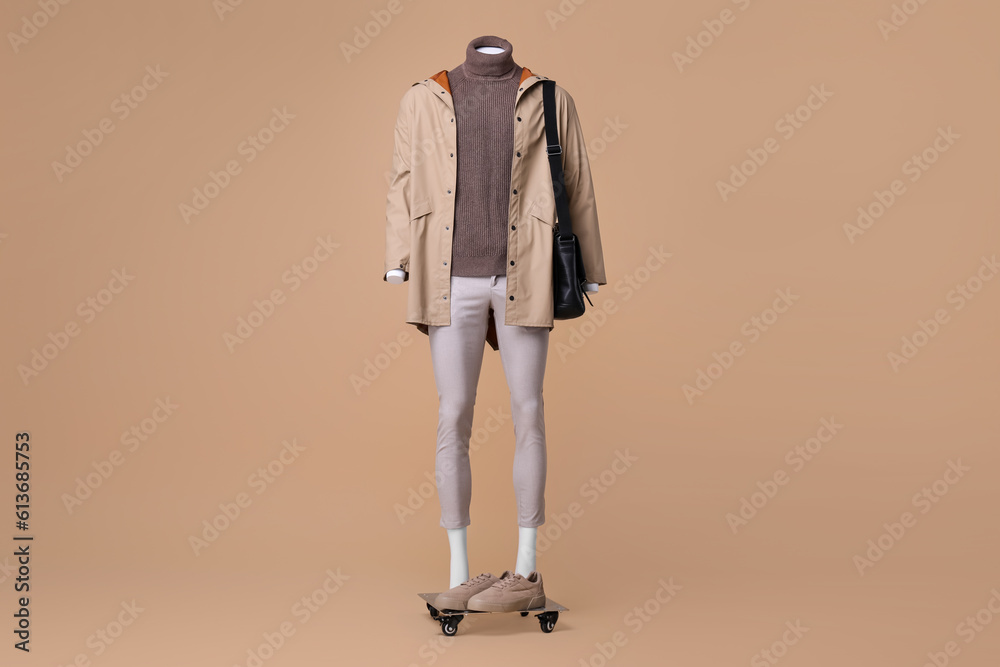 Fototapeta premium Male mannequin with bag dressed in stylish coat, turtleneck and pants on beige background