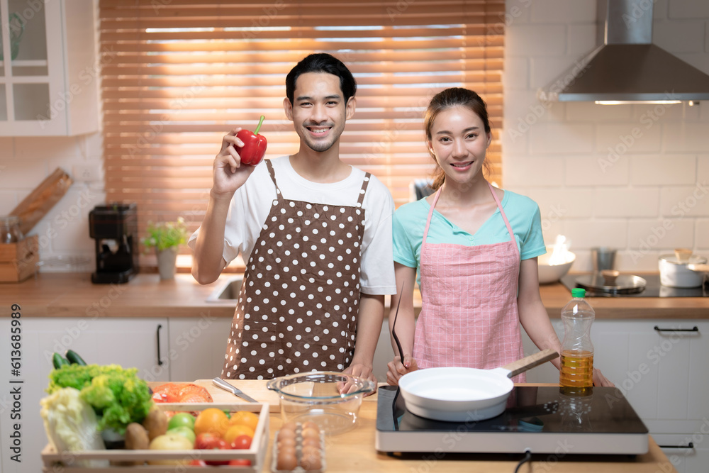 Happy Asian couple in the kitchen helping to cook dinner together.