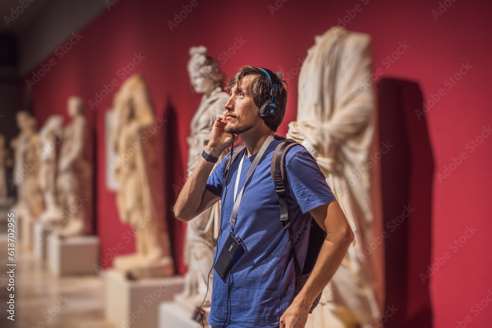 Fototapeta premium Portrait of contemporary man looking at sculptures and listening to audio guide at museum exhibition
