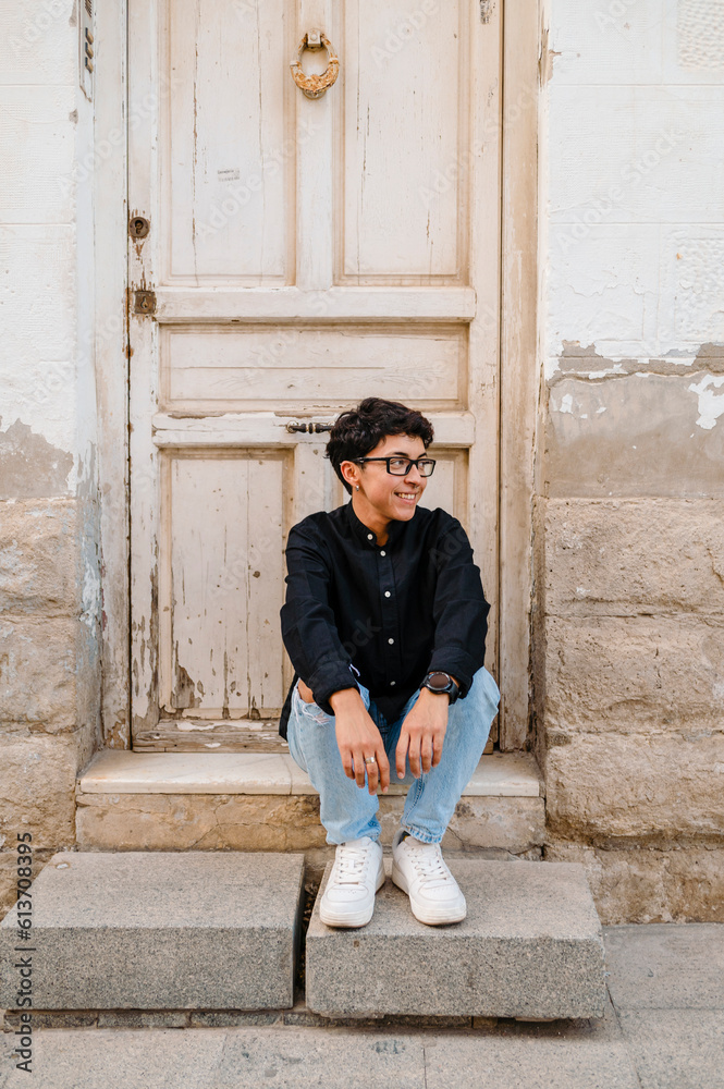 Young transgender man posing sitting on the front steps of a house. Young transgender man posing sitting on the front steps of a house.