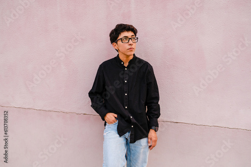 Young transgender man leaning on a wall while posing outdoors on the street.