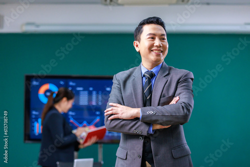 Portrait shot Millennial Asian professional successful male businessman ceo entrepreneur in formal business suit standing crossed arms smiling meeting room with male and female colleagues discussing
