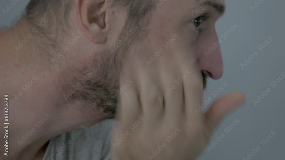A man is trimming his facial hair with an electric razor to look good. The close up shot shows a human's face while he is shaving his beard and trimming his look.