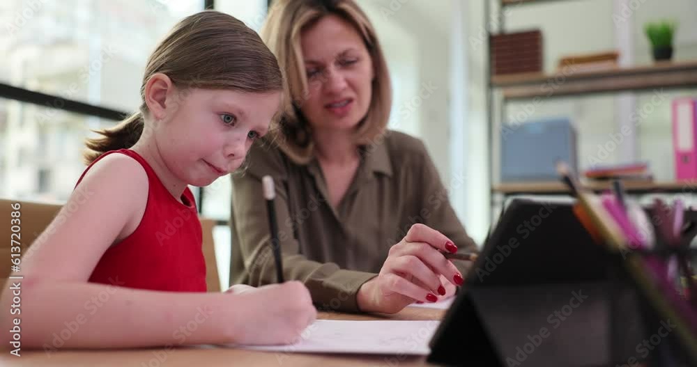 The girl in the class writes with a pencil, near the teacher, a close-up. Learning to write preschool children