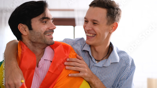 Two gay homosexual friends standing in arms with smiling faces and laughing joyfully, rainbow flag, gay pride or LGBTQ concept.