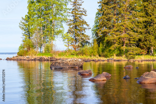 Landscape of the coastline of the lake with large stones, various tall trees. photo