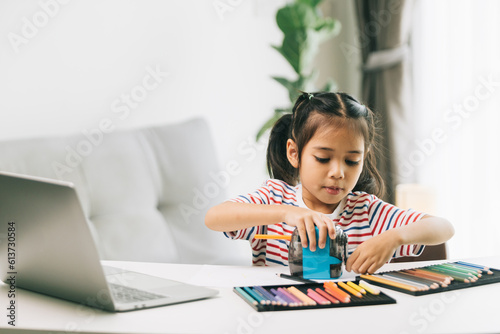 Cute asian little girl using color pencils and laptop at home