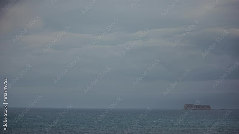 Tiny rocky island in middle of sea on dark moody day, time lapse view Tiny rocky island in middle of sea on dark moody day, time lapse view