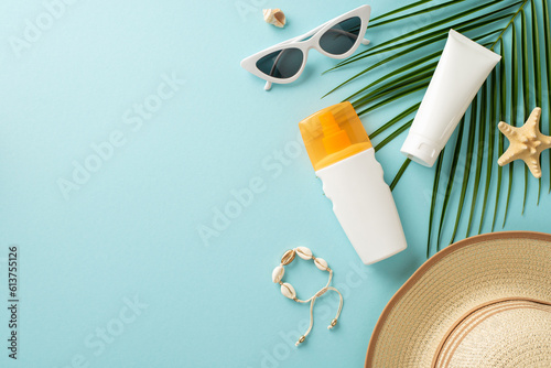 Embrace warmth of sun while protecting your skin. Top view of sunblock lotion and SPF cream tube without labels, eyeglasses, cap, shell bracelet, starfish, and a palm leaf on a pastel blue background