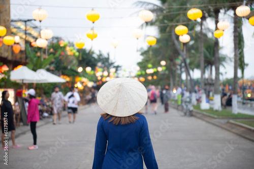 Tourist woman is wearing Non La (Vietnamese tradition hat) and looking colorful lanterns on the old street of Hoi An Ancient Town - UNESCO World Heritage village.