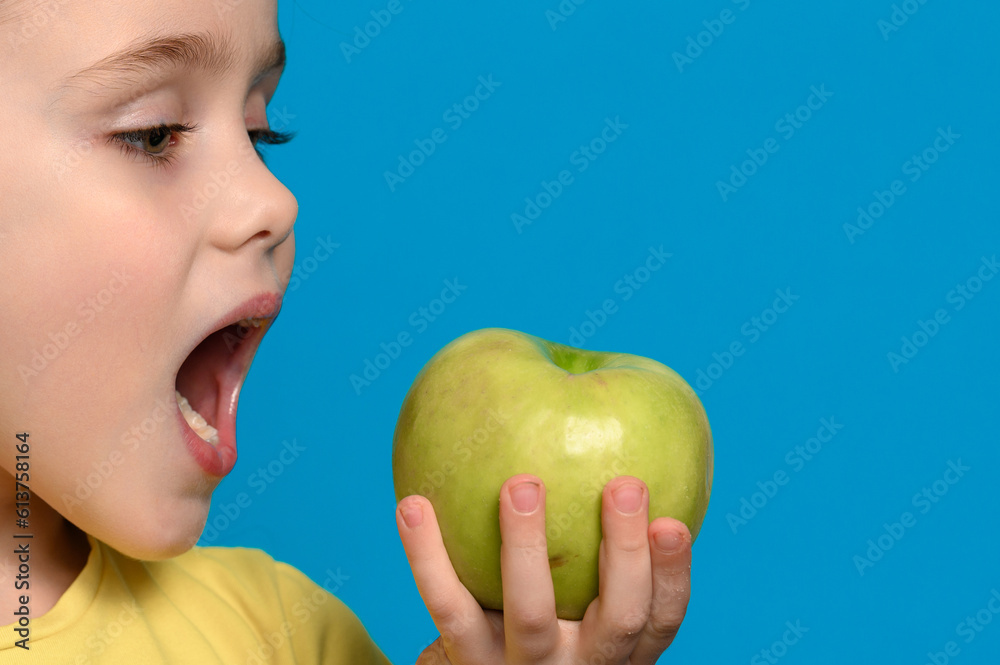 A little girl is holding and biting a green apple on a blue background. A little girl is holding and biting a green apple on a blue background.