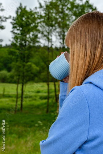 Kobieta pijąca herbatę z kubka w środku zielonego lasu