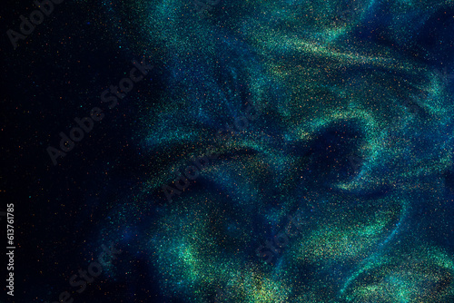 Various stains and overflows of gold particles in blue fluid with green tints. Golden particles dust and smooth defocused background. Liquid iridescent shiny backdrop with depth of field.