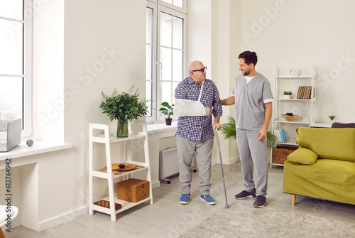 Doctor, nurse or caregiver taking care of an injured senior patient. Friendly young man in uniform talking to a fat old man who has a sling on his broken arm. Injury treatment, senior care concept