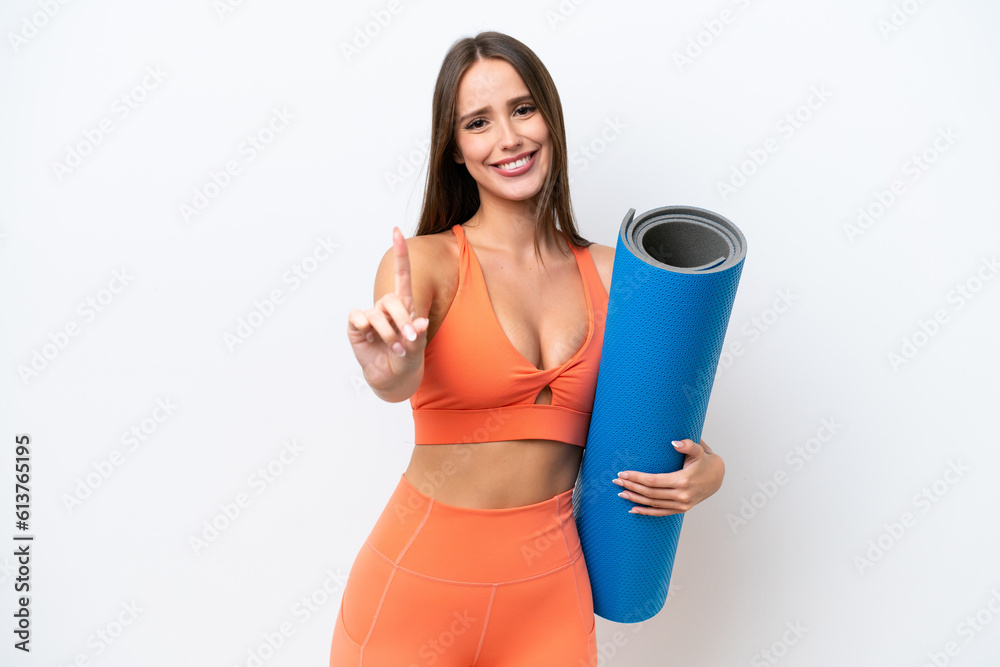 Young beautiful sport woman going to yoga classes while holding a mat isolated on white background showing and lifting a finger Young beautiful sport woman going to yoga classes while holding a mat isolated on white background showing and lifting a finger