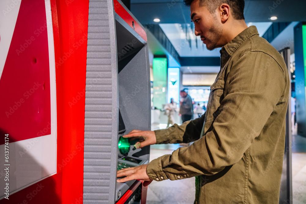 Ethnic man using ATM machine in shopping center