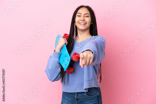 Teenager girl with braids over isolated pink background with a skate and pointing to the front