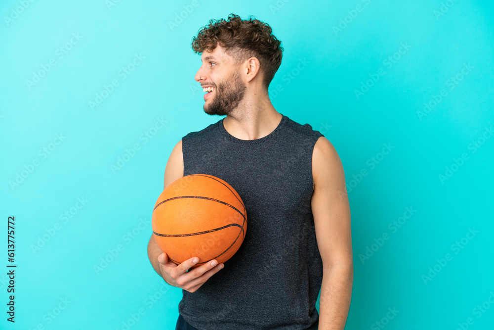 Handsome young man playing basketball isolated on blue background laughing in lateral position