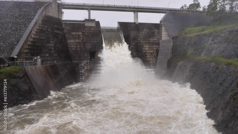 Wide handheld shot of Hinze Dam under heavy rain and water overflow
