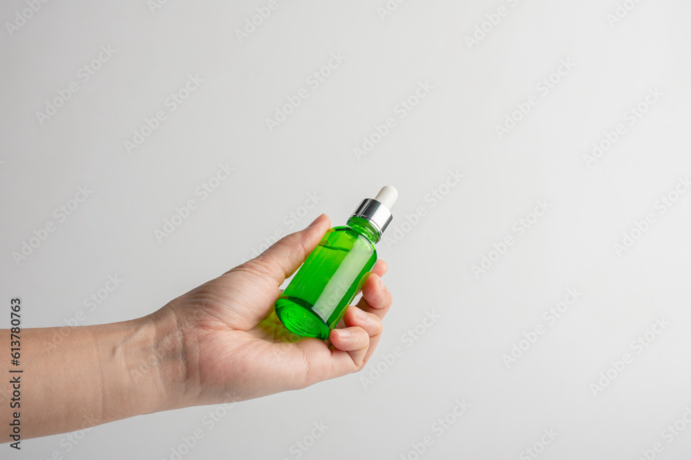 Hand holding up a green glass dropper bottle on white background