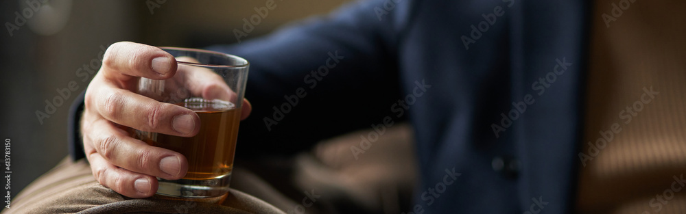 Successful middle aged business man holding glass of alcohol scotch whiskey in his hand while relaxing indoors. Focus on a drink Successful middle aged business man holding glass of alcohol scotch whiskey in his hand while relaxing indoors. Focus on a drink