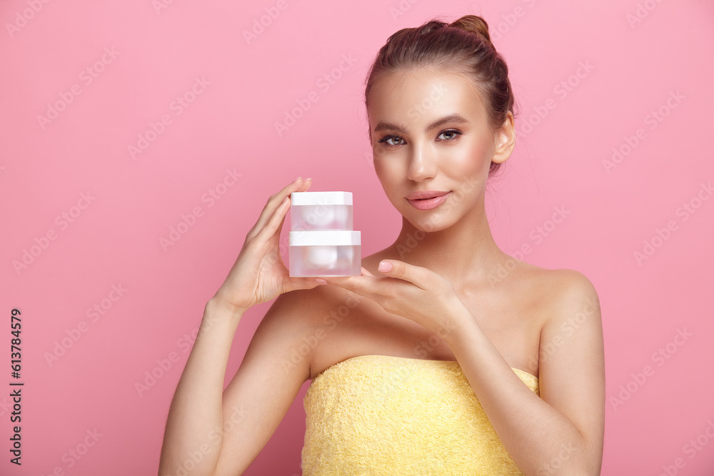 Pretty woman with bare shoulders holds cream on pink