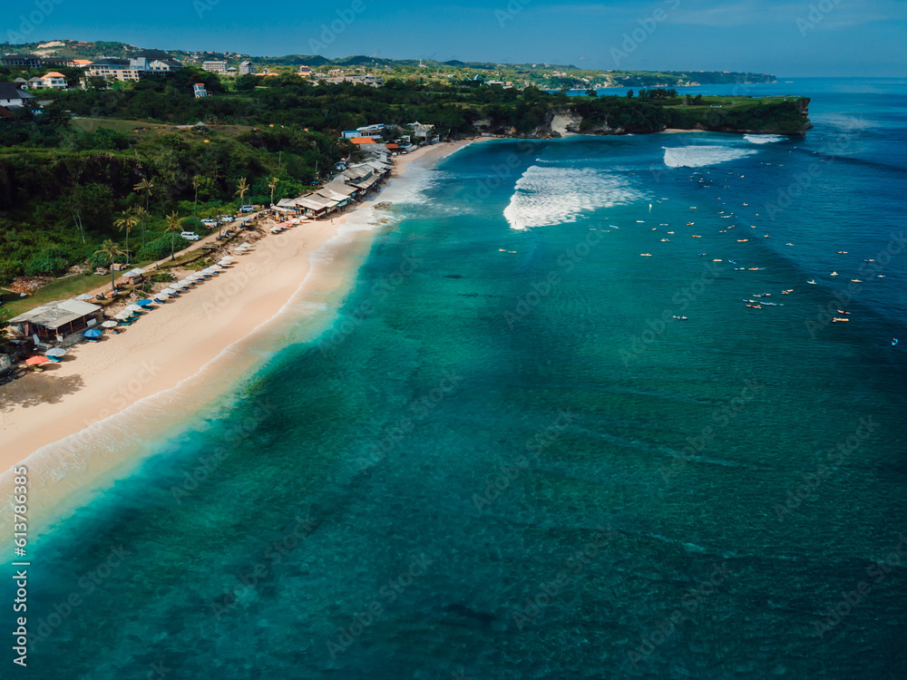 Popular holiday beach in Bali with surfing waves in turquoise ocean. Aerial view