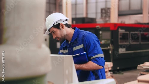Professional Engineer man in safety uniform writing record data on clipboard and using computer numerical control or CNC machine in warehouse at steel factory