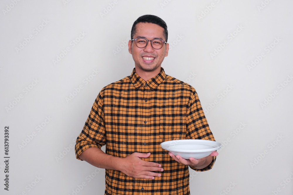 A man smiling with hand touhing his stomach and holding empty dinner plate A man smiling with hand touhing his stomach and holding empty dinner plate