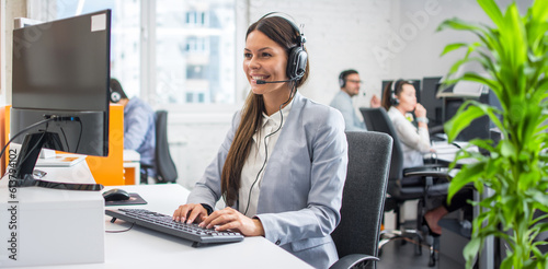 Beautiful young customer service representative wearing headset working on computer at cal center office.