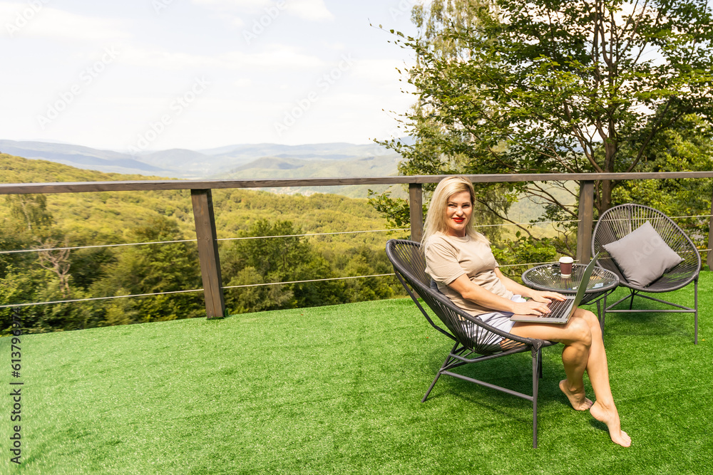 woman sitting on hotel balcony with laptop computer while working remote on freelance. mountains view woman sitting on hotel balcony with laptop computer while working remote on freelance. mountains view