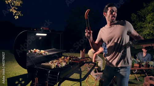 Man grilling barbecue for friends sitting in a circle campfire, Holiday and camping concept