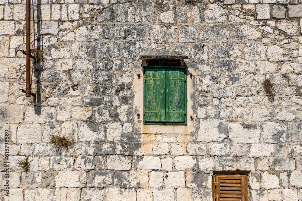 Typical old house with weathered closed green wooden shutters and stone wall, Rogoznica village, Dalmatia, Croatia