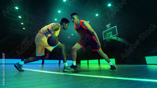 Young athletes, professional two basketball players of competitive teams in action with ball at 3d model sports arena.