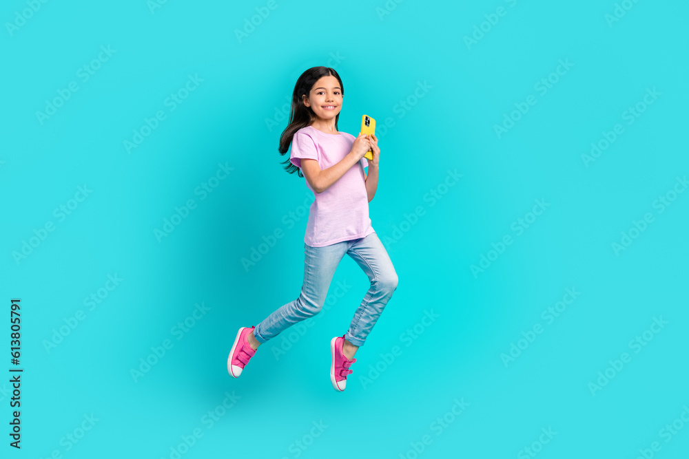 Full length body size photo of small funky girl jump hold smartphone wifi connection playing gadget games isolated on blue color background Full length body size photo of small funky girl jump hold smartphone wifi connection playing gadget games isolated on blue color background