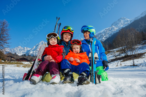 Family of mom and small kids sit with ski in snow over mountain