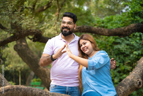 Young indian couple making home shape with hand at park