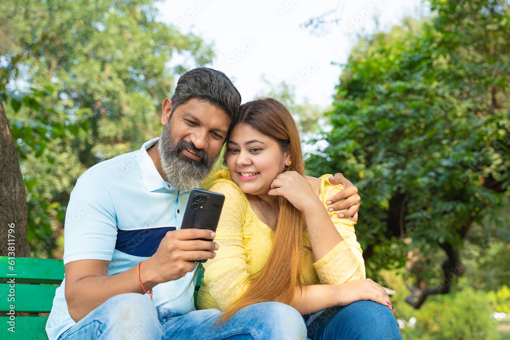Happy indian couple sitting at garden and watching some in smartphone. Happy indian couple sitting at garden and watching some in smartphone.