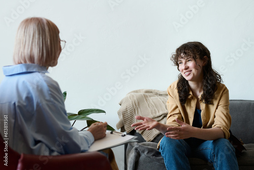 Young smiling woman talking to therapist while she making notes in document during psycho session