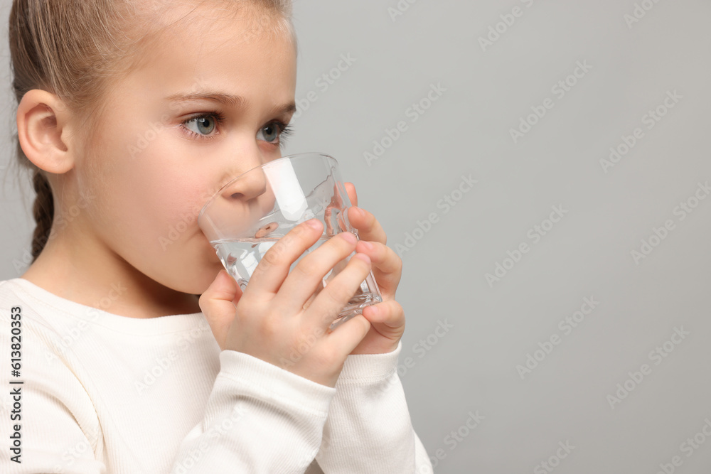 Cute little girl drinking fresh water from glass on light grey background, space for text Cute little girl drinking fresh water from glass on light grey background, space for text