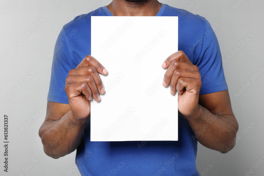 African American man holding sheet of paper on grey background, closeup. Mockup for design African American man holding sheet of paper on grey background, closeup. Mockup for design