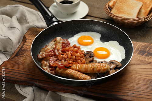 Frying pan with cooked traditional English breakfast on wooden table