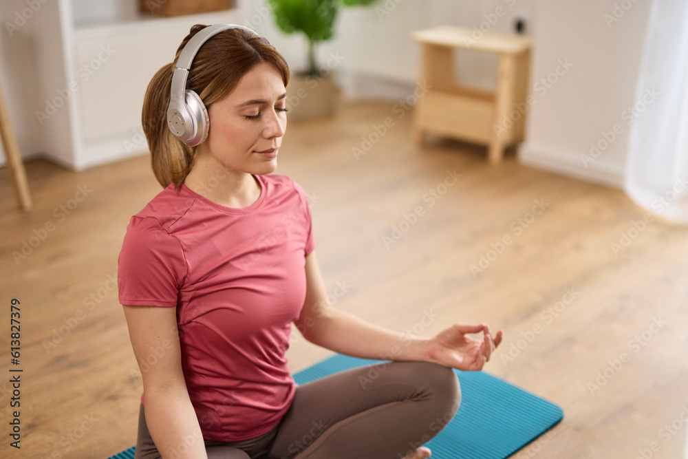 Beautiful young woman with headphones meditating on yoga mat at home Beautiful young woman with headphones meditating on yoga mat at home